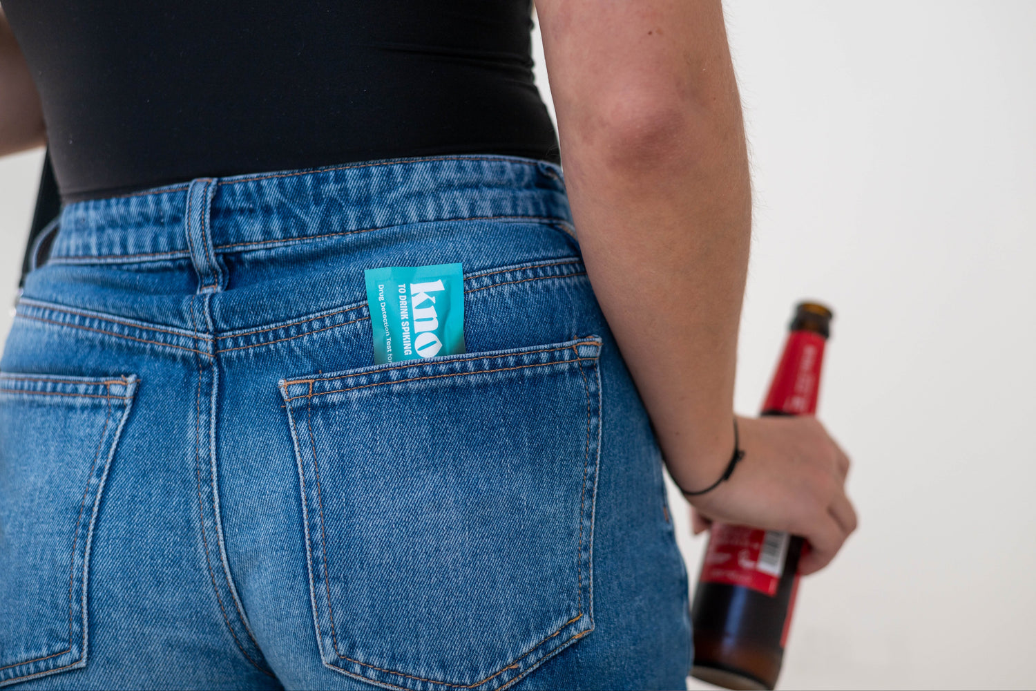 person holding a beer bottle with a Knope test in back pocket of their blue jeans