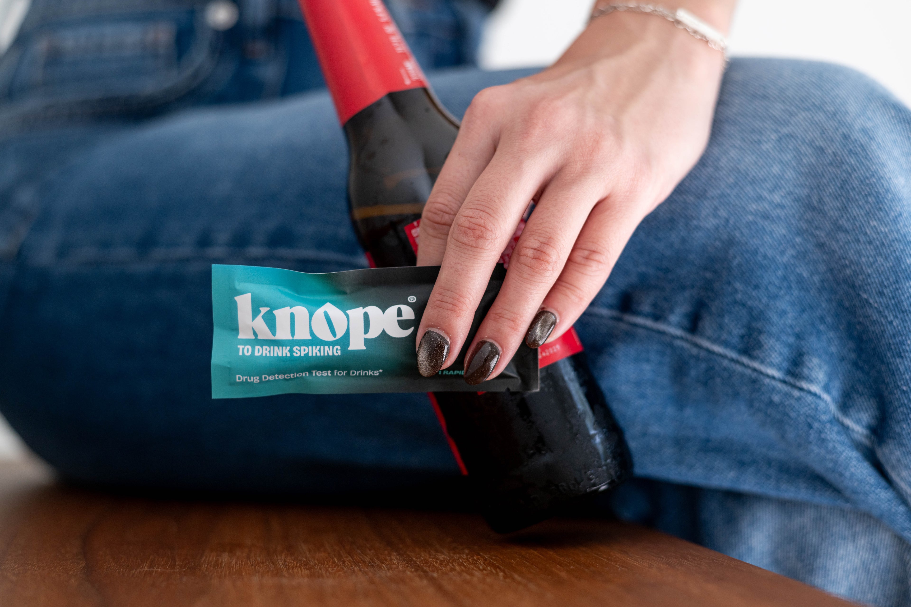 person holding a knope drug detection test for drinks and bottle of beer with legs crossed